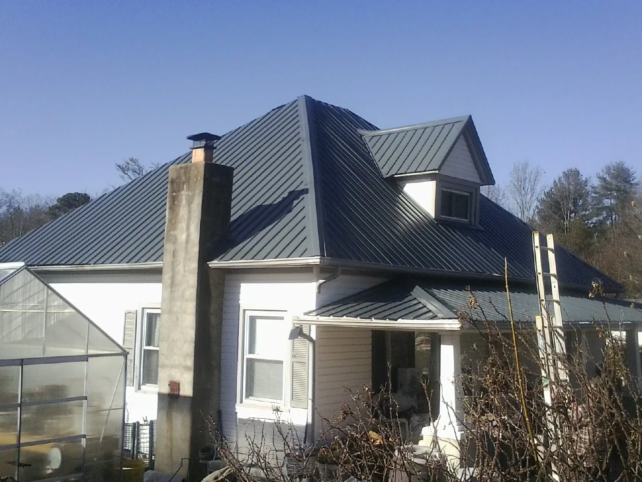 Dark blue standing seam metal roof on a white farmhouse with dormer — Slate & Tile Roof Repair by Roofing Brothers in Hallwood