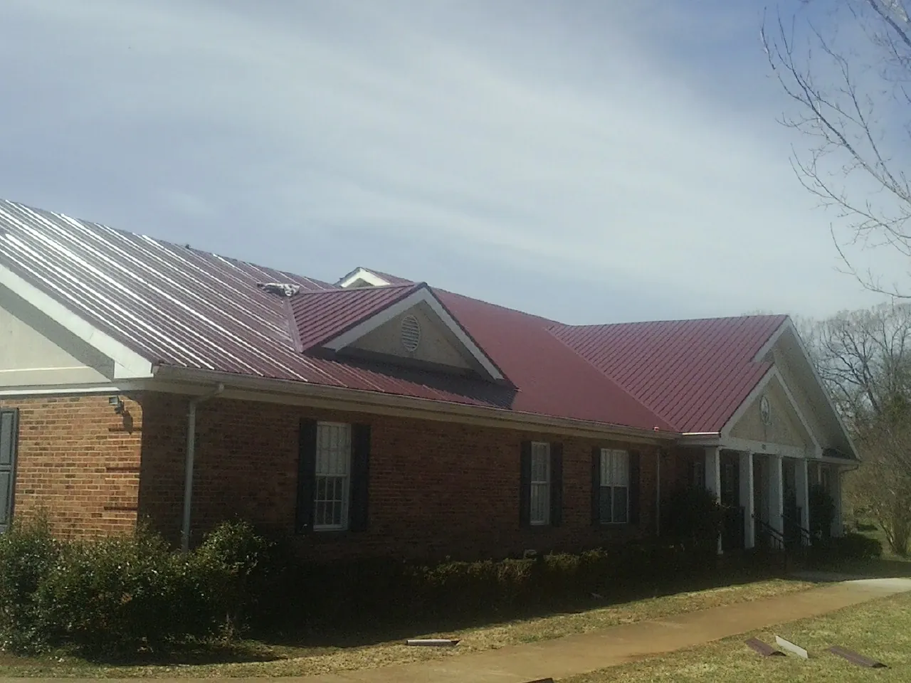 Red metal roof with gabled entries on a long brick building, from a Hail Damage Roof Repair job in Hallwood