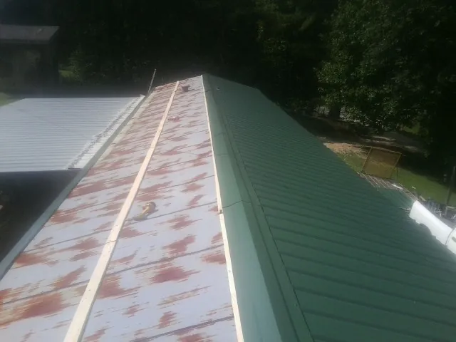 Old rusted panels beside newly installed green metal roofing — Wind Damage Roof Repair by Roofing Brothers in Hallwood
