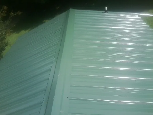New green metal panels meeting at the ridge of a roof — Flat Roof Repair work by our crew in Hallwood