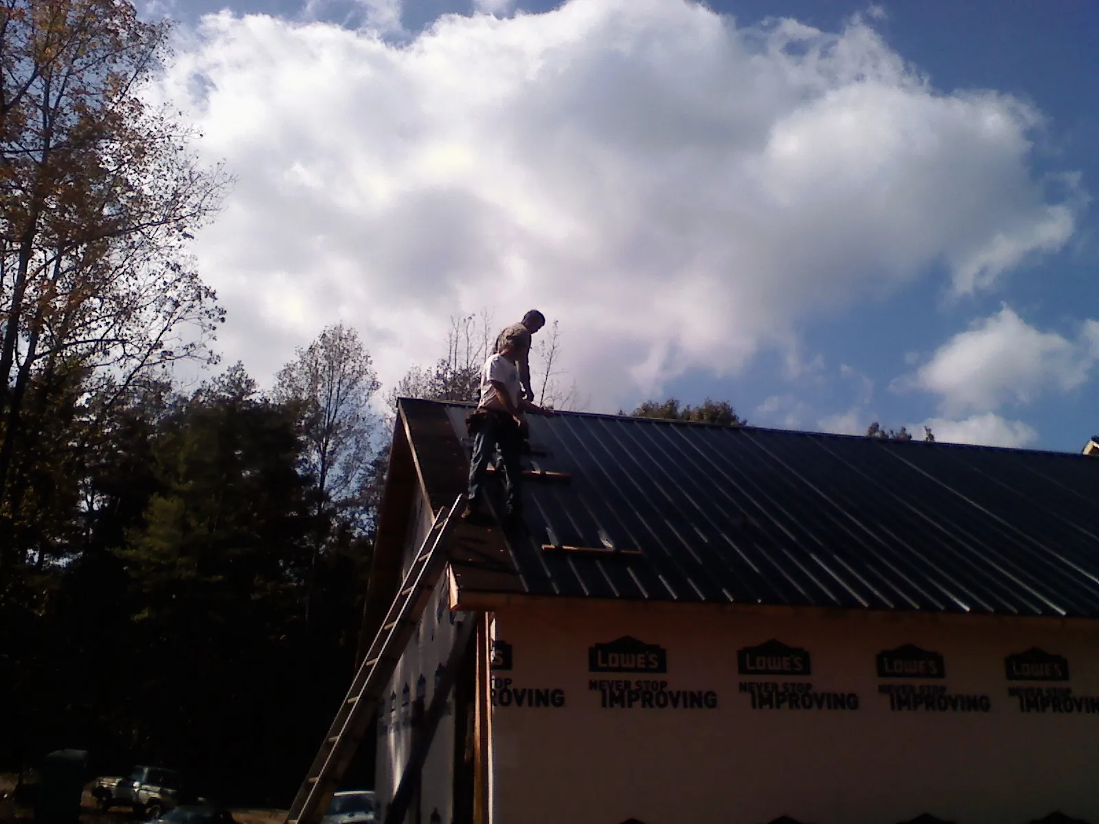 Roofer fastening dark metal panels high against a cloudy sky, from a Roof Inspection job in Hallwood