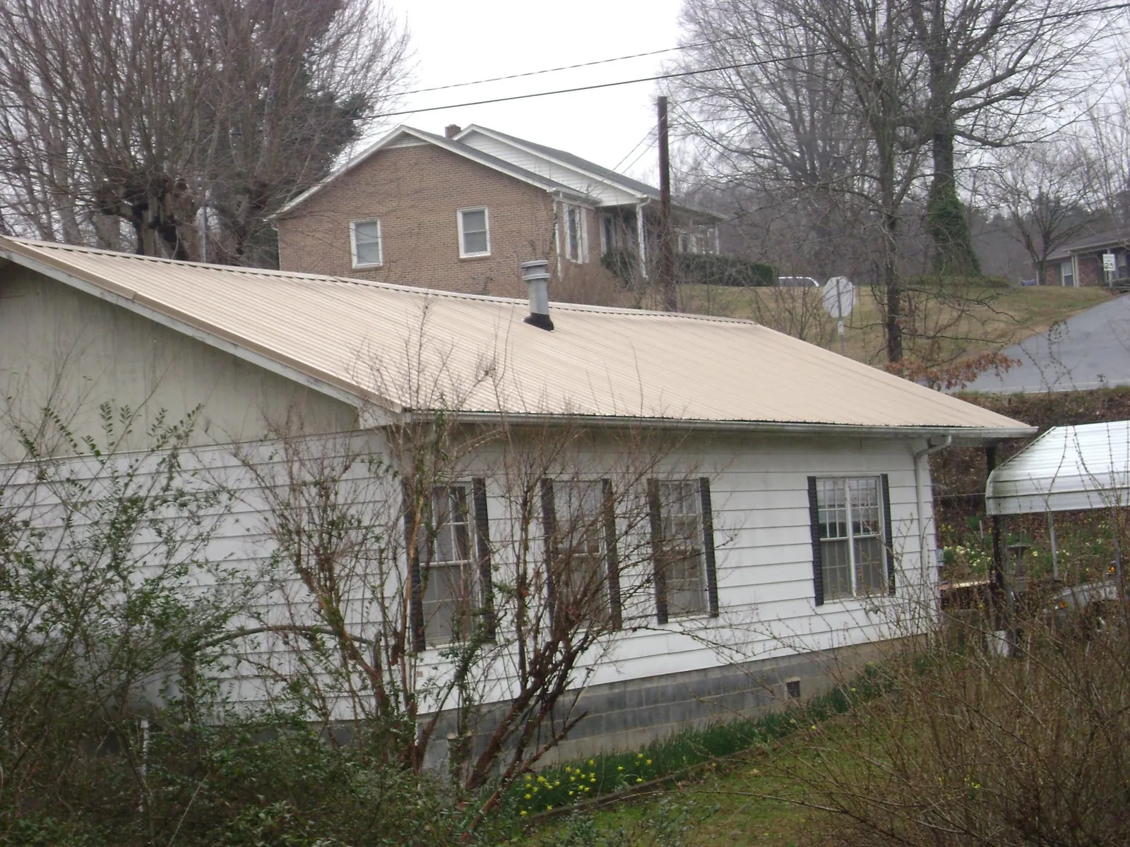 Tan metal roof on a white sided house set into a hillside — Commercial Roofing by Roofing Brothers in Hallwood